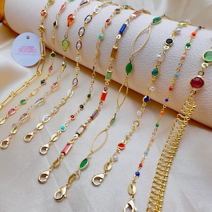 Op de afbeelding: Een verzameling van 12 gouden kettingen met verschillende gekleurde kralen en bedels. De kettingen zijn in verschillende stijlen, waaronder een delicate ketting, een dikke ketting en een ketting met een veerclip. De kralen zijn gemaakt van glas, parel en andere materialen. De bedels zijn in de vorm van vierkanten, ovalen en bladeren. Alle kettingen zijn ongeveer 45 cm lang.