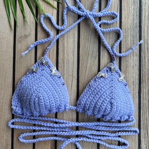 May include: A purple crocheted bikini top with silver butterfly embellishments. The top has adjustable straps and ties at the back.