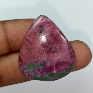 Könnte beinhalten: Ein rosa-grüner Edelstein-Cabochon in Tropfenform. Der Stein hat eine glatte, polierte Oberfläche und eine Vielzahl von Farben, darunter Rosa, Grün und Weiß.