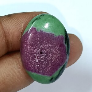 May include: Oval-shaped green and pink gemstone with a drilled hole. The gemstone has a swirling pattern of green and pink.