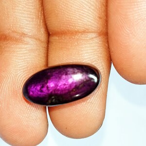 Pode incluir: Uma gema oval de cor p&uacute;rpura profunda com um acabamento brilhante e iridescente.