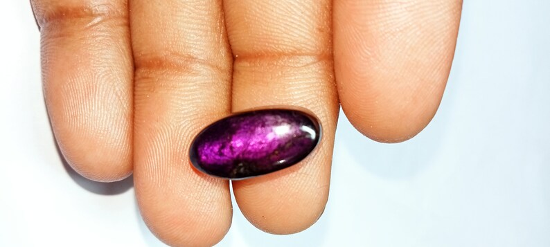 Pode incluir: Uma gema oval de cor p&uacute;rpura profunda com um acabamento brilhante e iridescente.