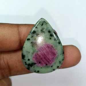 May include: A green and pink gemstone cabochon with black inclusions. The gemstone is in a teardrop shape and has a pink center.