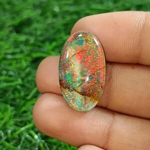 May include: A close-up of a colorful opal gemstone with a translucent, iridescent finish. The opal is oval-shaped and has a variety of colors, including red, orange, yellow, green, and blue.