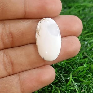 Puede incluir: Piedra preciosa blanca ovalada en cabujón con inclusiones marrones. La piedra preciosa está engastada en un anillo de plata.