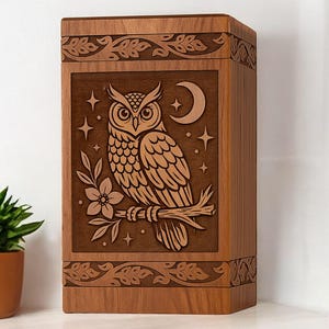 Könnte beinhalten: Holzkiste mit einem gravierten Eulen-Design. Die Eule sitzt auf einem Ast mit einer Blume, Mond und Sternen. Die Kiste hat dekorative Blattmuster an den oberen und unteren Kanten. Die Kiste ist aus Holz.