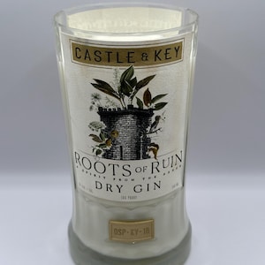 May include: A clear glass bottle with a white label that reads "CASTLE & KEY" and "ROOTS OF RUIN A SPIRIT FROM THE ASHES DRY GIN DSP-KY-18". The label features a drawing of a castle with a green leafy design.