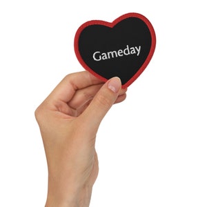 Op de afbeelding: Een rood hartvormig patch met een zwart midden en witte geborduurde tekst die "Gameday" luidt.