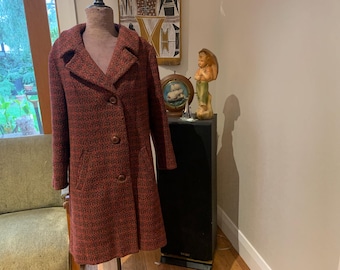 Op de afbeelding: Een vintage rood-zwarte tweed jas met een reverskraag en drie knopen. De jas wordt op een mannequin gepresenteerd. De jas heeft een klassiek, op maat gemaakt ontwerp en is waarschijnlijk uit het midden van de 20e eeuw.
