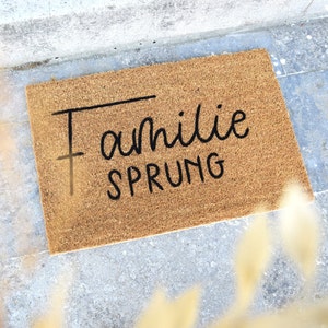 May include: A brown coir doormat with the text "Familie Sprung" in black lettering.