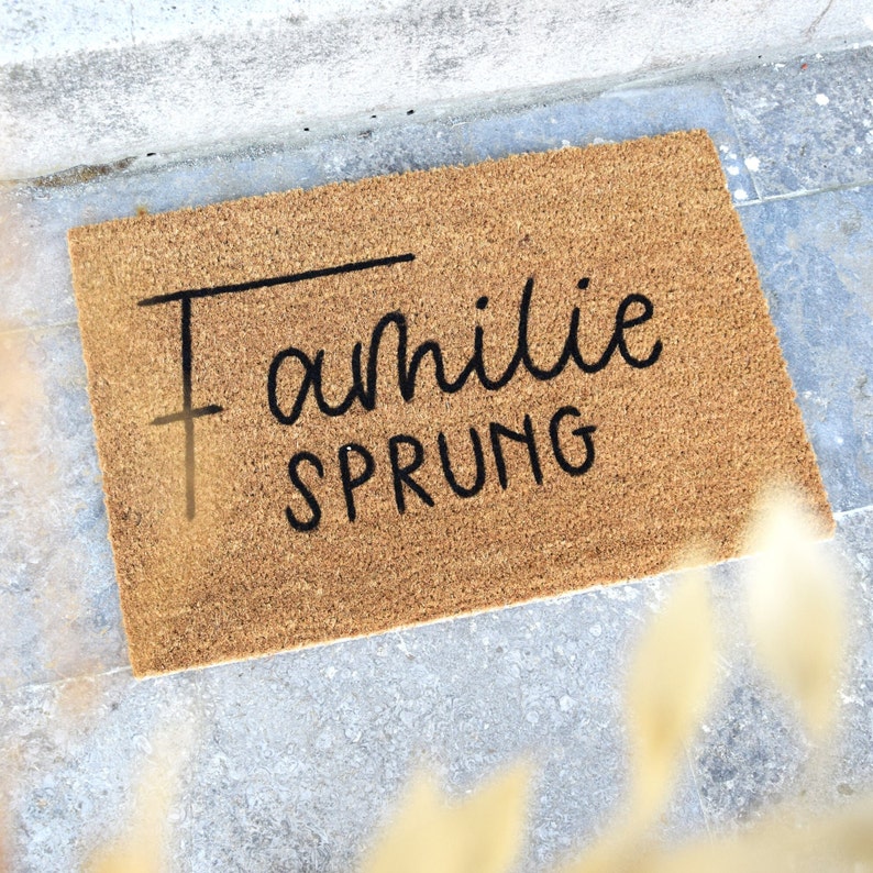 May include: A brown coir doormat with the text "Familie Sprung" in black lettering.