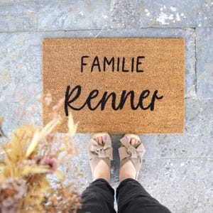 Könnte beinhalten: Eine braune Kokosmatte mit dem Text "Familie Renner" in schwarzen Buchstaben.