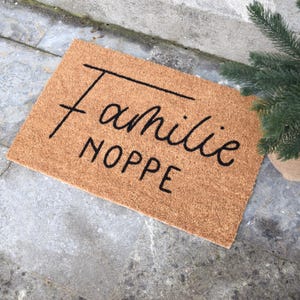 May include: A brown coir doormat with the text "Familie Noppe" in black cursive lettering.