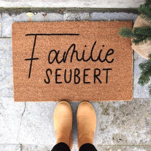 May include: A brown coir doormat with the text "Familie Seubert" in black lettering.
