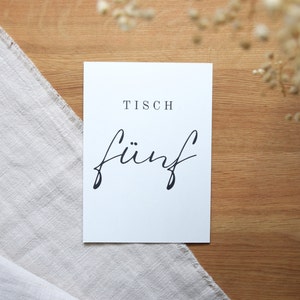 May include: White card with black text that reads "Tisch f&uuml;nf" which translates to "Table five" in English.