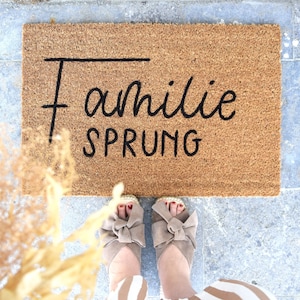 May include: A brown coir doormat with the text "Familie Sprung" in black lettering.