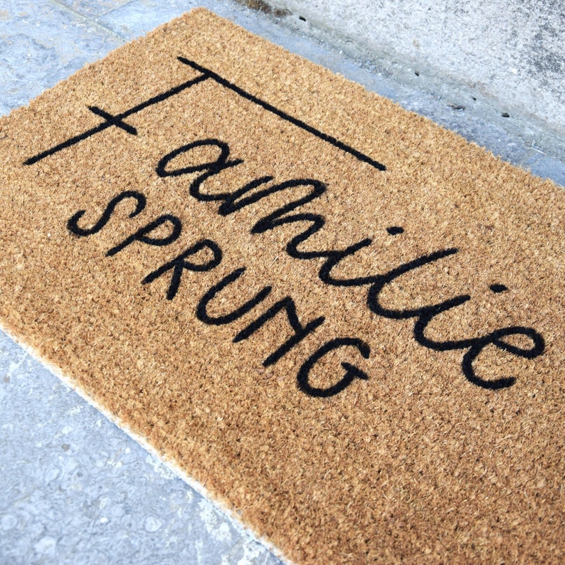 May include: A brown coir doormat with the text "family sprung" written in black cursive.