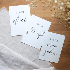 May include: Three white cards with black text. The cards are labelled "Tisch drei", "Tisch f&uuml;nf", and "Tisch vierzehn".