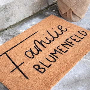 May include: A brown coir doormat with the text "Familie Blumenfeld" in black cursive lettering.