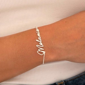 May include: A silver name bracelet with the name "Melanie" written in cursive.