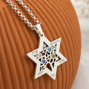 Può includere: Una collana con ciondolo a forma di Stella di David color argento con un design ad albero intagliato al centro. Il ciondolo è impreziosito da quattro piccole pietre preziose rotonde nei colori blu, azzurro, verde e trasparente. Testo ebraico inciso.