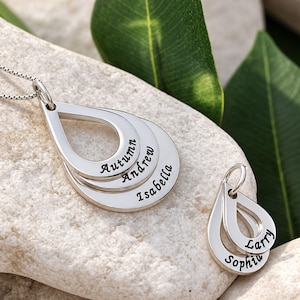 May include: A silver-toned necklace featuring three stacked teardrop-shaped pendants engraved with the names Autumn, Andrew, and Isabella, alongside a separate smaller charm with two teardrop pendants engraved with the names Larry and Sophia.