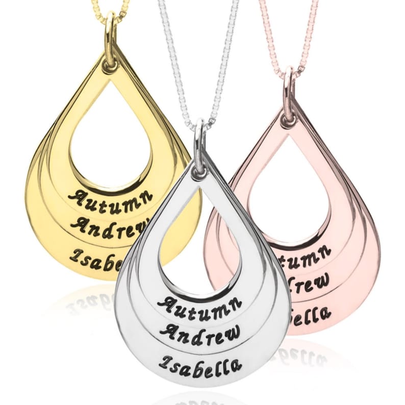 May include: Three teardrop-shaped pendants on delicate chains in gold, silver, and rose gold tones. Each pendant features three horizontal cutouts engraved with the names Autumn, Andrew, and Isabella in a black script font, suspended from thin chains.