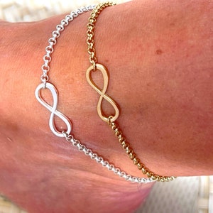May include: Two infinity symbol anklets, one silver and one gold, on a person's ankle.