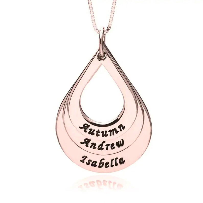 May include: A rose gold-toned teardrop-shaped pendant necklace featuring three stacked, open-center layers. The bottom section of each layer is engraved with the names Autumn, Andrew, and Isabella in a dark, cursive script font.