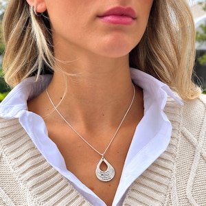 May include: A silver-toned necklace featuring a teardrop-shaped pendant composed of three stacked, graduated layers. Each layer is engraved with a name, specifically Autumn, Andrew, and Isabella, suspended from a thin, delicate silver chain.