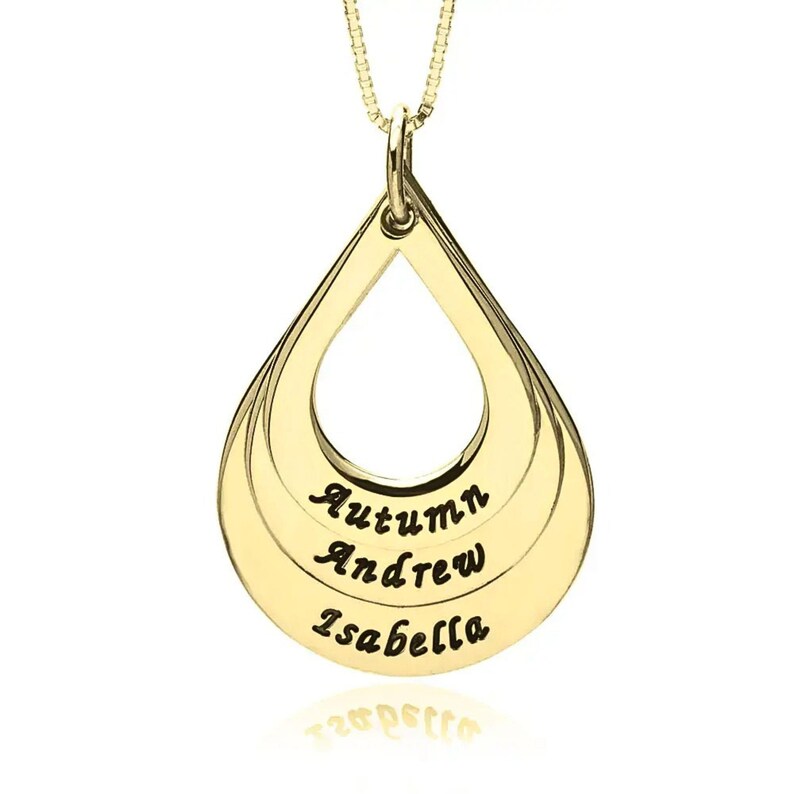 May include: A gold-toned teardrop-shaped pendant necklace featuring three horizontal engraved lines. The names Autumn, Andrew, and Isabella are inscribed in a black script font across the center of the pendant, which hangs from a delicate chain.
