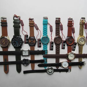 May include: A collection of wristwatches with various band colors, including brown, black, green, and turquoise. The watches have different face designs and are displayed on a white surface. Each watch has a tag attached.