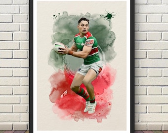 May include: A framed watercolor print of a rugby player in action, holding the ball. The player is wearing a green, red, and white uniform. The background features green and red watercolor splashes. The print is set against a white brick wall.