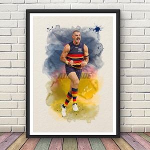 May include: A framed art print featuring a watercolour-style illustration of an Australian rules football player in a navy, red, and yellow uniform. The player is shown mid-stride with a celebratory expression, wearing number 13 and white shoes.