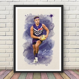 May include: A framed print depicting an athlete in a purple and white uniform, holding a yellow ball, rendered in a watercolor style. The artwork features a purple watercolor background and the text "#16 Murphy Reid".