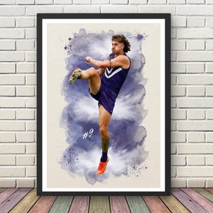May include: A framed watercolour print depicting a football player mid-kick. The player is in a purple uniform, number 9 visible. The artwork has a blue watercolour splash effect against a light beige background.