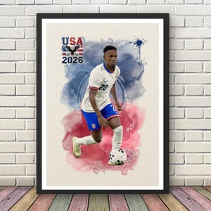 Pode incluir: Impressão emoldurada com um jogador de futebol com uma camisa branca com o número 20, calções azuis e meias brancas, driblando uma bola de futebol. O fundo tem respingos de aquarela vermelhos e azuis, com o texto "USA 2026" e uma águia.