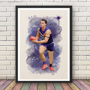 May include: A framed watercolour print of a football player in a purple and white kit, holding a football. The artwork features a purple watercolour background and the text "EST 1994" and "#3" and "Caleb Serong".