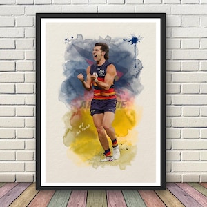 May include: A framed art print featuring a watercolour-style illustration of an Australian rules football player in a navy, red, and yellow uniform with the number 8 and the name Josh Rachele printed in white text on a cream-coloured background.