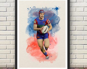 May include: A framed art print featuring a rugby player in a blue and red jersey and shorts, wearing a headguard, running while holding a white Steeden rugby ball. The background consists of blue and red watercolor splashes on a cream paper.