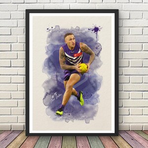 May include: Framed watercolour print of a football player in a purple and white uniform, holding a yellow ball. The artwork features a watercolour background with the text "EST. 1994" and the player's number and name.
