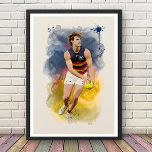 May include: A framed art print featuring a watercolor-style illustration of an Australian rules football player in a navy, red, and yellow jersey with the Toyota logo, white shorts, and white sneakers, holding a yellow ball with the number 25 visible.