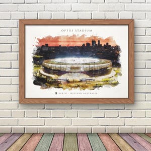 May include: Framed watercolour print of Optus Stadium in Perth, Western Australia. The artwork shows the stadium against a sunset and city skyline. The text "OPTUS STADIUM" and "PERTH - WESTERN AUSTRALIA" are displayed on the print.