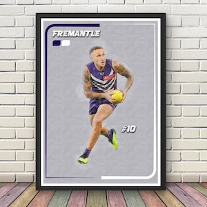 May include: Framed artwork depicting an athlete in a purple and white uniform, holding a yellow ball. The word "FREMANTLE" is at the top, with the number "10" in the bottom right corner. The artwork is presented in a black frame, suitable for wall display.