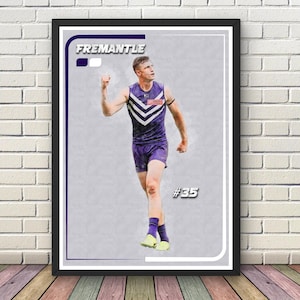 May include: Framed print with a watercolour illustration of an athlete in a purple and white uniform. The word "FREMANTLE" is at the top, with the number "35" on the bottom right. The athlete is celebrating a victory.