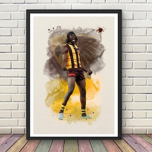 May include: A framed art print featuring a watercolor-style illustration of an Australian rules football player in a brown and gold striped jersey and shorts, with the text #18 Mabior Chol visible on the lower left side against a textured background.