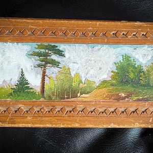 Op de afbeelding: Een houten doos met een gesneden ontwerp rond de randen. Het deksel heeft een geschilderd tafereel van een bos met bomen en een bewolkte lucht.