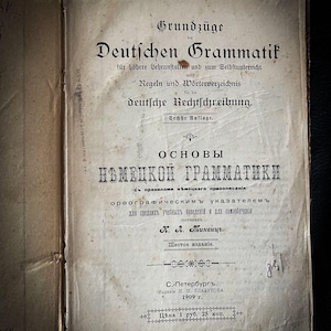 May include: A book cover with the title "Grundzüge der Deutschen Grammatik" and the subtitle "Regeln und Wörterverzeichnis für die deutsche Rechtschreibung." The book is the sixth edition and is titled "Основы Немецкой Грамматики" in Russian.