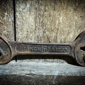 Op de afbeelding: Een roestige moersleutel met een grote, open kop en een kleinere, gesloten kop. De moersleutel is gegraveerd met de tekst "Французский завод" in het Cyrillisch schrift.