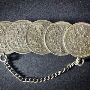 Op de afbeelding: Een zilveren ketting met vijf verbonden zilveren munten met een ontwerp van een dubbelkoppige adelaar.